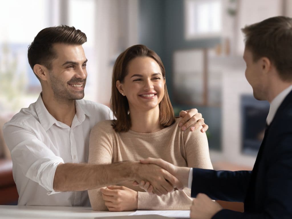 smiling young couple shakes hands with man in suit in home