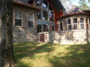 An outside view of a brick home, complete with glass windows and doors. The sun is shining onto the home.